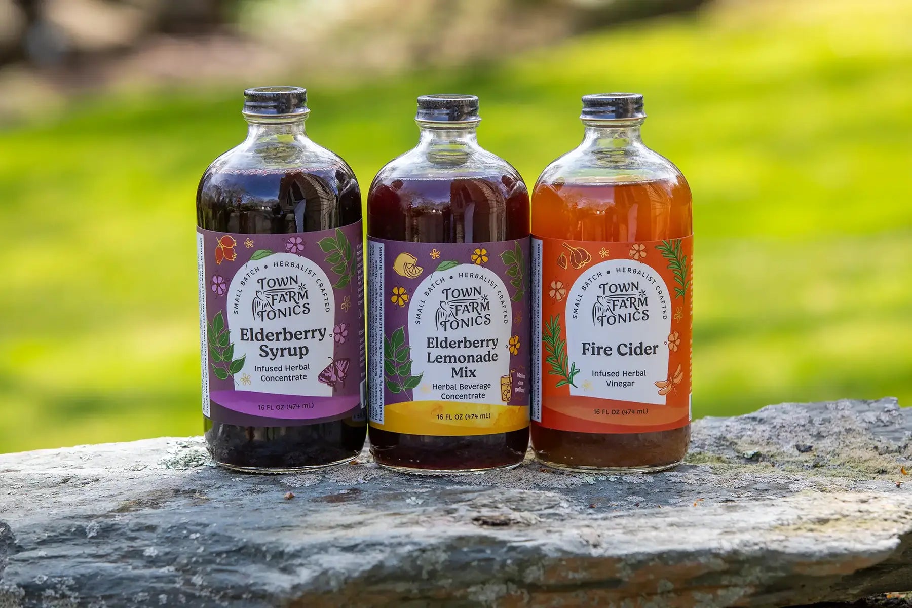 Three bottles of Town Farm Tonics on a stone surface with a blurred green background