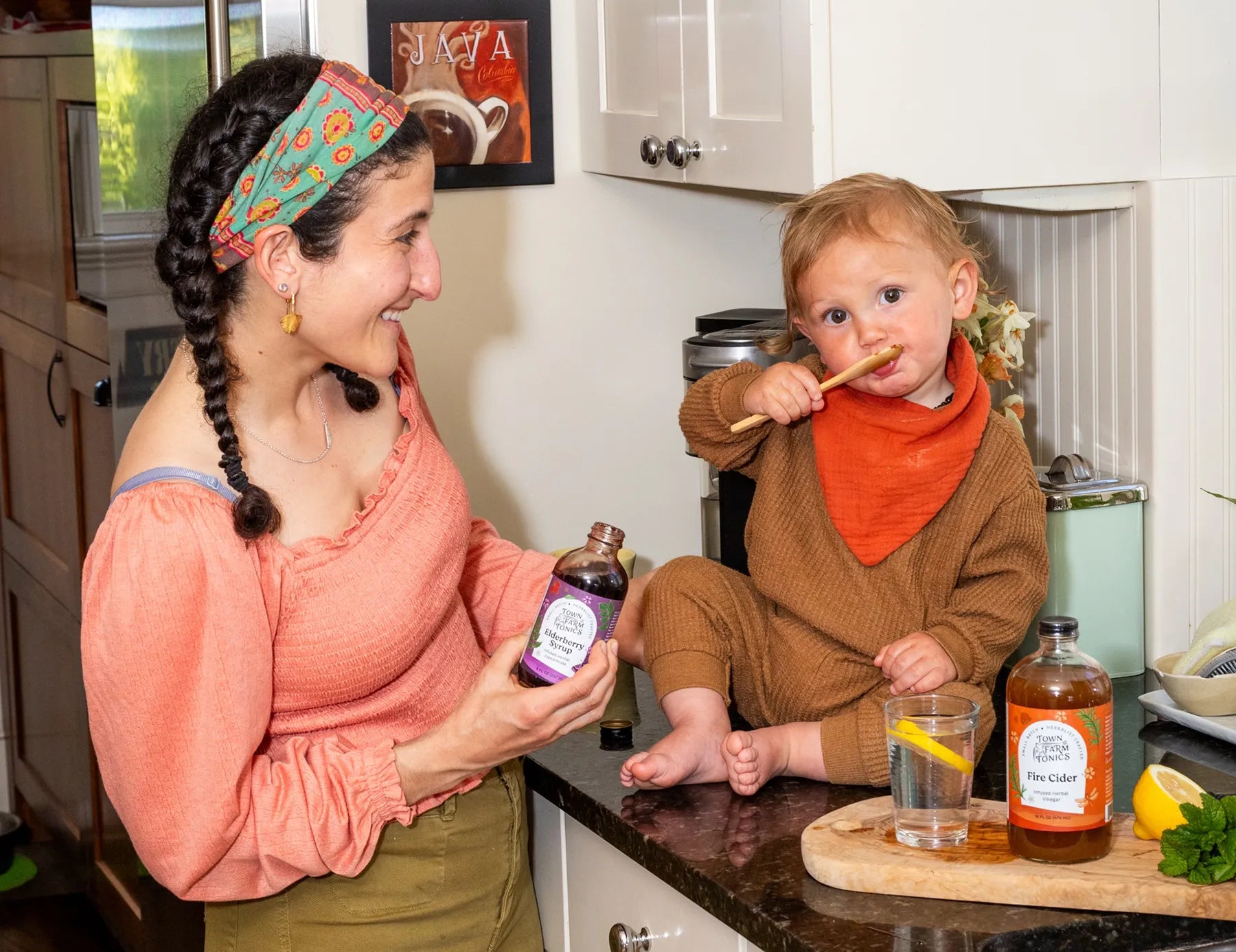 Woman owner smiling at her child licking spoon with tonic on it