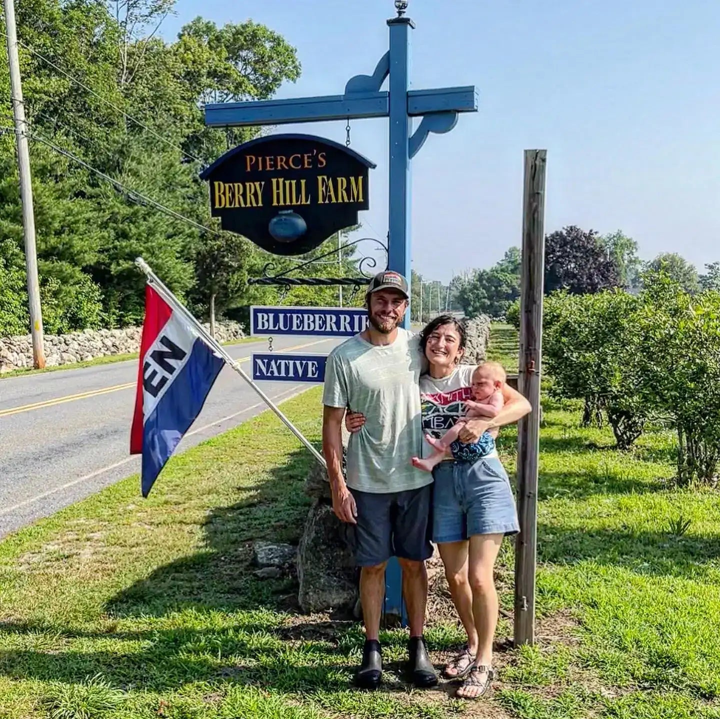 Owners posing with baby in front of a farm sign for Pierce's Berry Hill Farm.