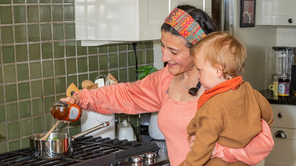 Woman holding child while making tonic over stove